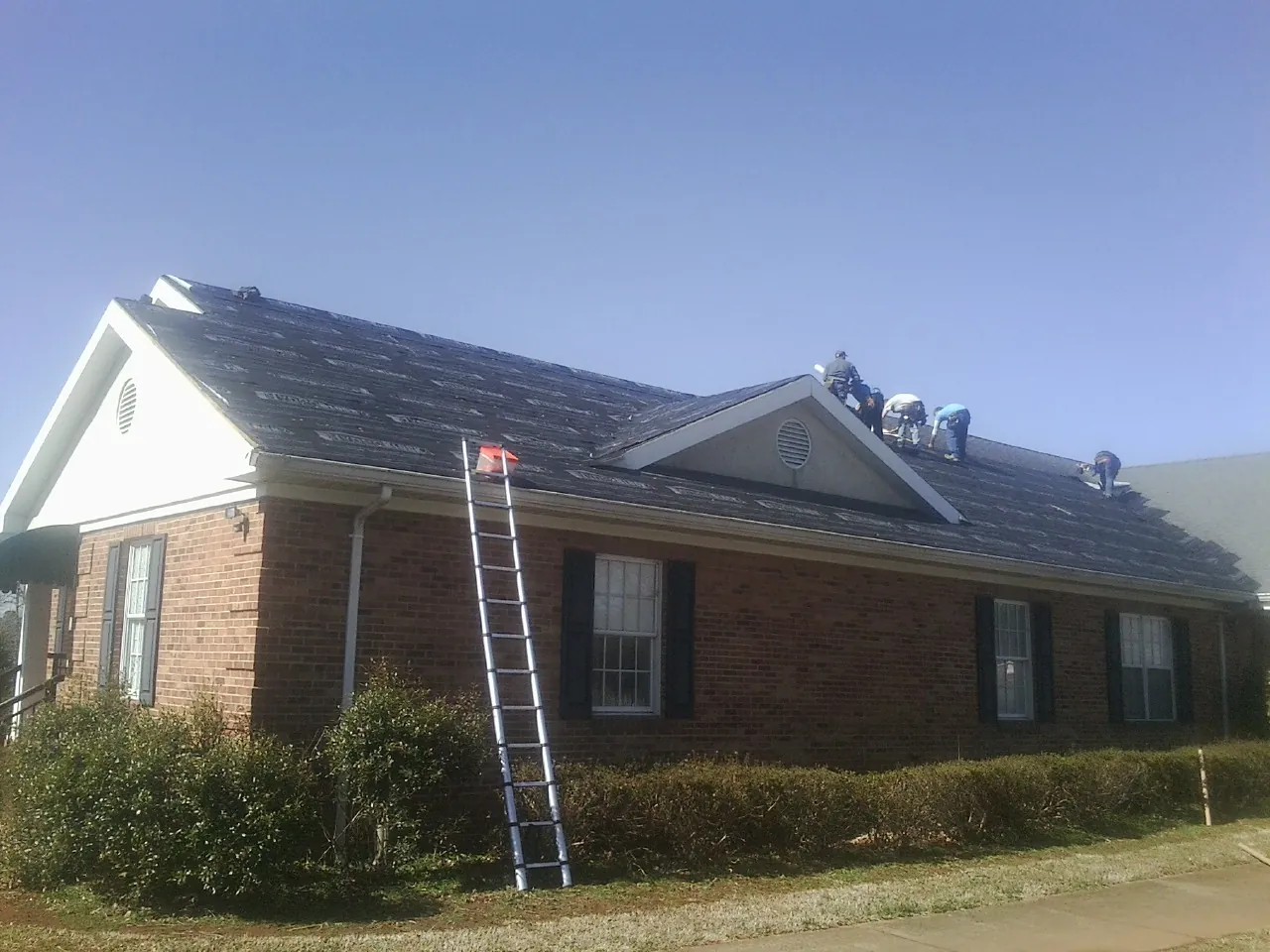 Crew tearing shingles off a brick ranch roof with a ladder set — Emergency Roof Repair work by our crew in Ceresco