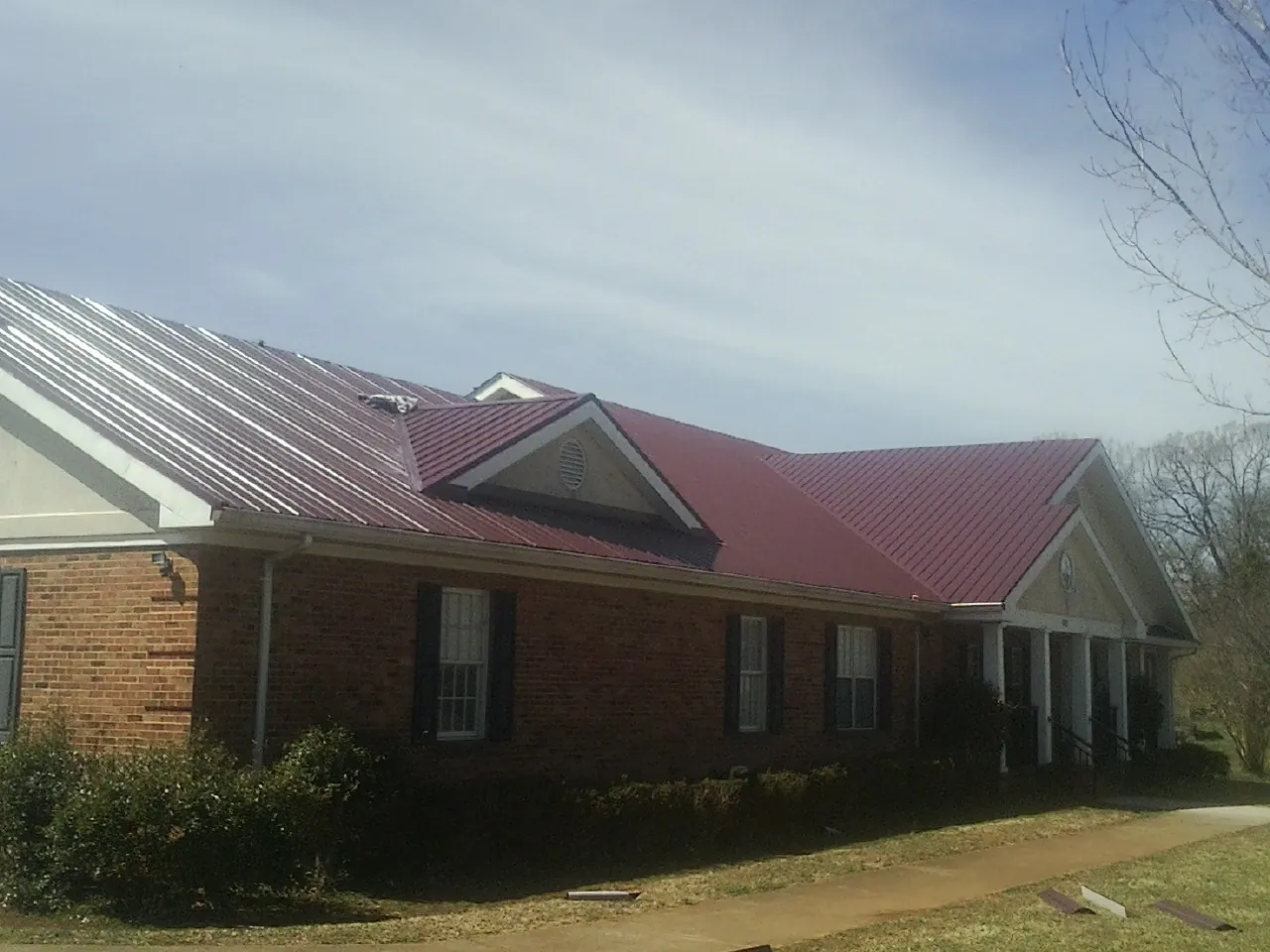 Red metal roof with gabled entries on a long brick building, from a Hail Damage Roof Repair job in Ceresco