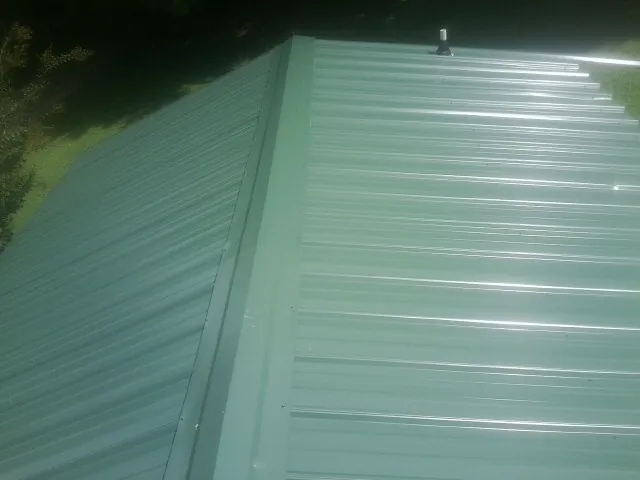 New green metal panels meeting at the ridge of a roof — Flat Roof Repair work by our crew in Ceresco