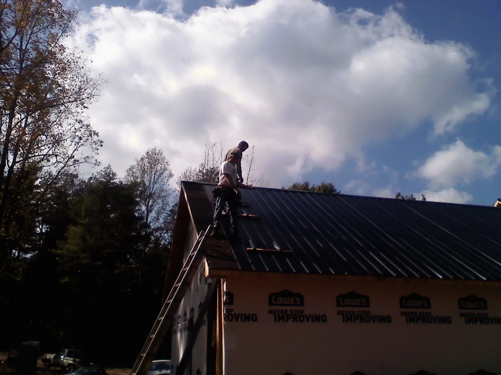Roofer fastening dark metal panels high against a cloudy sky in Ceresco
