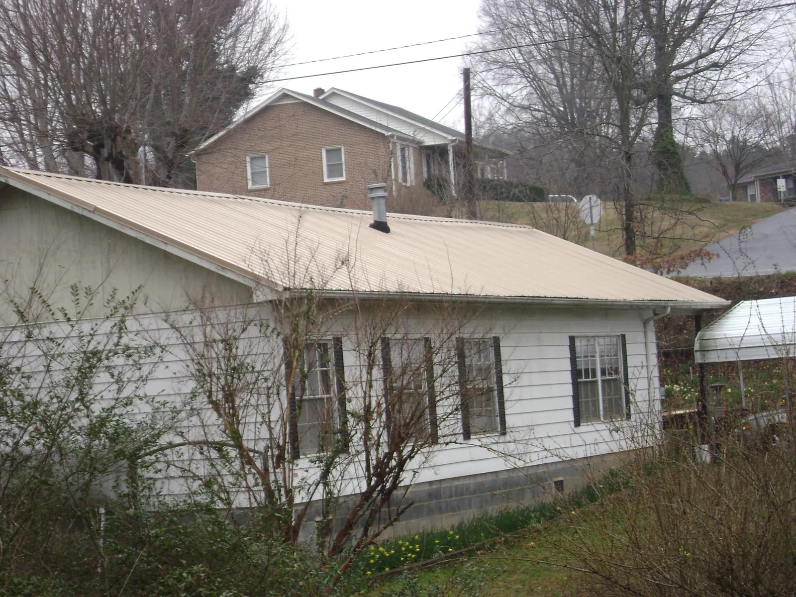 Tan metal roof on a white sided house set into a hillside — Commercial Roofing by Roofing Brothers in Ceresco